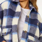 Campera tipo camisa de Rip Curl, confeccionada en tejido de punto con diseño de cuadros en tonos azul, celeste y blanco. Presenta cuello clásico, cierre frontal con botones, bolsillos delanteros y mangas largas con puños abotonados.