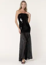 Vestido largo de fiesta con escote strapless. La parte superior presenta un diseño ajustado cubierto de lentejuelas negras, mientras que la parte inferior está confeccionada en chiffon plisado con paneles godet que aportan volumen y movimiento.