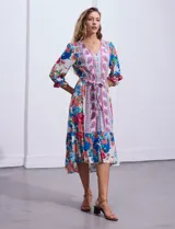 Vestido midi con estampado floral en tonos azules, rojos y blancos. Tiene escote en V, mangas 3/4 con puños fruncidos, cintura elastizada con lazo de ajuste y falda con volantes.