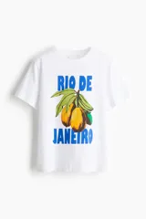 Remera blanca de corte holgado con cuello redondo y mangas cortas. Presenta un estampado central con la frase 'Rio de Janeiro' en letras azules y una ilustración de frutas tropicales.