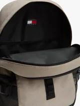 Mochila outdoor Tommy Jeans color beige con base negra, bolsillo principal con cierre, bolsillos laterales de red y asa superior. Cuenta con detalles distintivos de la marca y logo bordado en el frente.