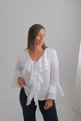 Blusa blanca de manga larga con volados en el cuello y en los puños. Presenta un cierre frontal con botones y un diseño fluido.