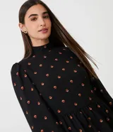 Vestido corto negro de chiffon con estampado de pequeños corazones naranjas, cuello alto, mangas largas abullonadas y falda con volados en capas.