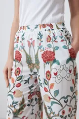 Pantalón de corte recto con estampado floral en tonos naranja, rojo, verde y marrón sobre fondo blanco. Presenta cintura elástica y ruedo con diseño geométrico.