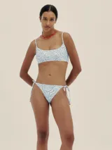 Conjunto de bikini con estampado de cebra en tonos celeste y blanco. El corpiño es de corte recto con tirantes finos y la bombacha es tipo colaless con tiras ajustables en los laterales.