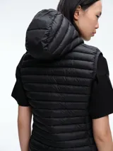 Chaleco acolchado ultraligero de nylon color negro, con cierre frontal y capucha integrada. Diseño de la línea Giga con relleno sintético Plumtech para aislamiento térmico.