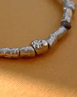 Collar artesanal compuesto por piezas metálicas irregulares con acabado dorado, ensartadas en un cordón de hilo de algodón natural. Presenta un sistema de nudo corredizo para ajustar el largo.