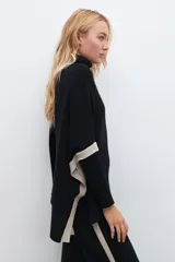 Polera negra de cuello alto, corte oversized y mangas largas con detalle de franjas color crema en los hombros.