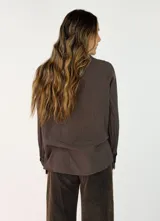 Camisa de corte oversize color beige, con cuello clásico, cierre frontal de botones y detalle de flores de tela aplicadas en el pecho.
