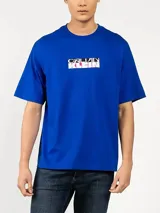 Remera de algodón azul con cuello redondo y corte relajado, que presenta un estampado gráfico con el logo de la marca en el pecho.