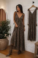 Vestido largo amplio de color marrón con estampado tipo paisley, escote en V pronunciado y tirantes regulables con borlas en los extremos.