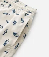 Bermuda de baño para hombre, color crema, con estampado repetitivo de peces azules. Presenta cintura elástica con cordón de ajuste y forro interior de malla.