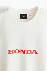 Remera de algodón color blanco con cuello redondo y estampado frontal con el logo de Honda en color rojo.