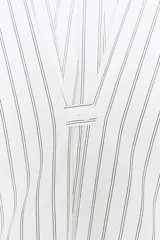 Camisa blanca de manga larga con cuello solapa y rayas verticales finas en color gris o celeste pálido. Presenta un calce oversize y cierre frontal con botones.