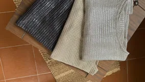 Blusa negra metalizada con escote bote que puede usarse recto o caído en un hombro y mangas largas acampanadas.