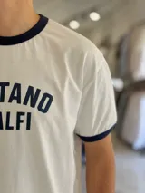 Remera de algodón pesado de corte oversize en color blanco, con cuello redondo y ribetes en las mangas de color azul marino. Cuenta con un estampado frontal con el texto "POSITANO AMALFI".