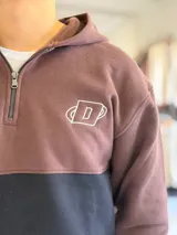 Hoodie de felpa con capucha y medio cierre frontal, diseño en bloques de color celeste y blanco, con bordados decorativos en el pecho.