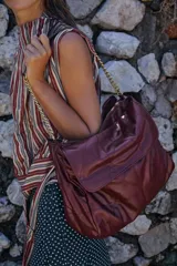 Bolso tipo shopper color borravino con diseño acolchado y pespuntes en rombos. Cuenta con solapa frontal y una correa de hombro que combina material sintético con una cadena metálica dorada.