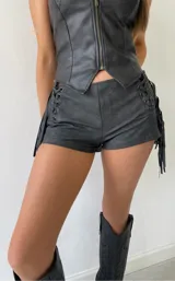 Short de cuero sintético color gris oscuro, con diseño de cordones laterales y flecos decorativos. Presenta un corte ajustado y estilo western.