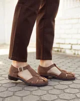 Sandalias de cuero gamuzado color marrón, tipo romanas, con tiras entrelazadas, talón cerrado y tira ajustable con hebilla metálica en el tobillo.