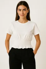 Remera blanca de algodón con cuello redondo, manga corta y sección inferior con smock elástico que ajusta la prenda al cuerpo y crea un pequeño volante en el ruedo.