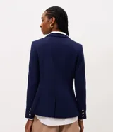 Blazer cruzado de sastrería en color azul marino, con corte slim y estructura entallada. Presenta solapas de muesca, cierre frontal con seis botones dorados metálicos con relieve, bolsillos con solapa en los laterales y mangas largas.