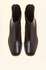 Bota de caña media confeccionada en cuero vacuno negro, con diseño minimalista y cierre trasero. Presenta un taco cilíndrico de madera tallada y punta cuadrada.