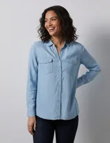 Camisa de manga larga en tela denim de color azul medio, con cuello clásico, botones frontales y dos bolsillos de parche con solapa en el pecho.