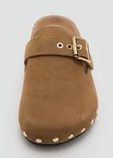 Mocasines destalonados de piel bovina color marrón con tachas metálicas doradas alrededor de la suela y una tira en el empeine con hebilla ajustable.