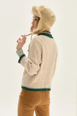 Sweater de punto con diseño de ochos en color crudo, con cuello polo y tapeta de botones en contraste verde. Presenta bordado en el pecho, puños y ruedo acanalados con detalles de rayas en verde.