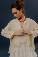 Chaqueta de lino color beige, de calce relajado, con escote en V, cierre frontal con botones y bolsillos frontales amplios.