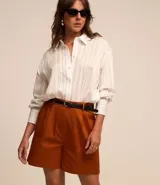 Short de vestir color beige, con cintura alta, pliegues frontales, cinturón de cuero sintético con hebilla metálica y cierre frontal con botón y cremallera.