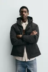 Parka técnica de corte relajado con interior ligeramente acolchado. Presenta cuello subido con capucha ajustable, cierre frontal con cremallera oculta por solapa con botones a presión, y cuatro bolsillos frontales de plastrón con solapa. Incluye cintura ajustable con cordón interior, puños con rib y aberturas laterales con cremallera en el bajo.