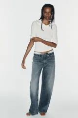 Jeans de mezclilla de tiro medio, corte wide leg y diseño relaxed. Presenta detalles rotos y desgastados en las piernas, y una cinturilla doblada superpuesta con trabillas y cierre frontal con cremallera y botón metálico.