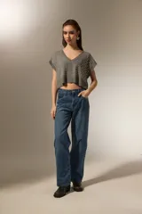 Chaleco de punto gris con cuello en V, diseño sin mangas y corte cropped. Presenta apliques de tachas metálicas plateadas distribuidas por toda la parte frontal y borde acanalado en el ruedo.