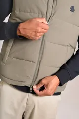 Chaleco puffer de corte regular, color beige, con cierre frontal y cuello alto. Presenta un diseño acolchado horizontal y logo bordado en el pecho.