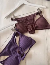 Bikini color marrón oscuro con corpiño tipo top texturizado, con hebilla ovalada marrón en el centro y tirantes finos. La bombacha es colaless entera con frunces en los costados. Incluye tazas soft removibles.