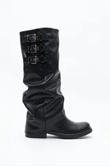 Bota de caña alta color negro, con diseño utilitario, puntera redondeada y taco bajo. Presenta un efecto fruncido en la caña y tres hebillas metálicas decorativas.