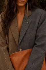 Blazer oversize de diseño bicolor con paneles asimétricos en tweed de cuadros, uno en tonos marrones y otro en tonos azulados. Presenta solapas clásicas, cierre frontal con botón de strass y un pin decorativo en forma de perro salchicha.