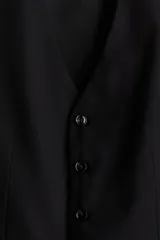 Chaleco de traje formal con cierre frontal de cinco botones y dos bolsillos delanteros ribeteados. Presenta un corte ajustado, forro interior y espalda con tejido brillante y trabilla ajustable.