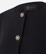 Saco corto de crepé en color negro, con cuello redondo, cierre frontal de botones metálicos y bolsillos con solapa en el frente. Presenta mangas largas y un diseño estructurado.