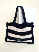 Bolso tipo tote tejido a crochet con hilo de algodón, con diseño a rayas horizontales en blanco y negro. Cuenta con manijas reforzadas y etiqueta de la marca Cilento.