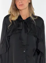Camisa de satén color naranja óxido, con cuello mao y lazo para anudar. Presenta volados decorativos en el frente y en las mangas, las cuales son largas y terminan en puños abotonados.