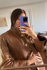 Tapado largo de cuero ovino color caramelo con cuello de piel sintética desmontable, detalles de pasamanería a tono en hombros y espalda y botones de guampa.