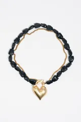 Collar de doble cadena, una de eslabones dorados y otra de piedras negras irregulares, con un dije central en forma de corazón dorado y cierre tipo T.