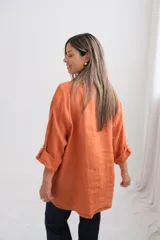 Camisa de lino color terracota, de corte holgado y diseño oversize. Presenta cuello clásico, cierre frontal con botones de nácar, bolsillo en el pecho y mangas largas con sistema de ajuste mediante trabilla y botón.