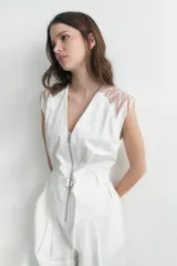 Mono largo blanco con cierre frontal, cinturón con hebilla metálica y detalles de tul en los hombros.