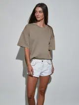 Short de jean blanco con tachas doradas decorativas en los bolsillos delanteros y en los laterales, talle medio y cierre frontal con botón y cremallera.