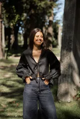 Blusa blanca de lino con mangas largas abullonadas, escote en V con lazo de ajuste frontal y detalles de puntilla en los bordes.