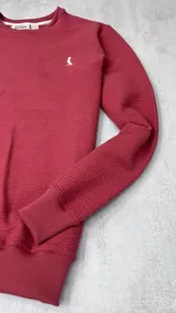 Buzo rojo de algodón texturizado, cuello redondo y mangas largas.